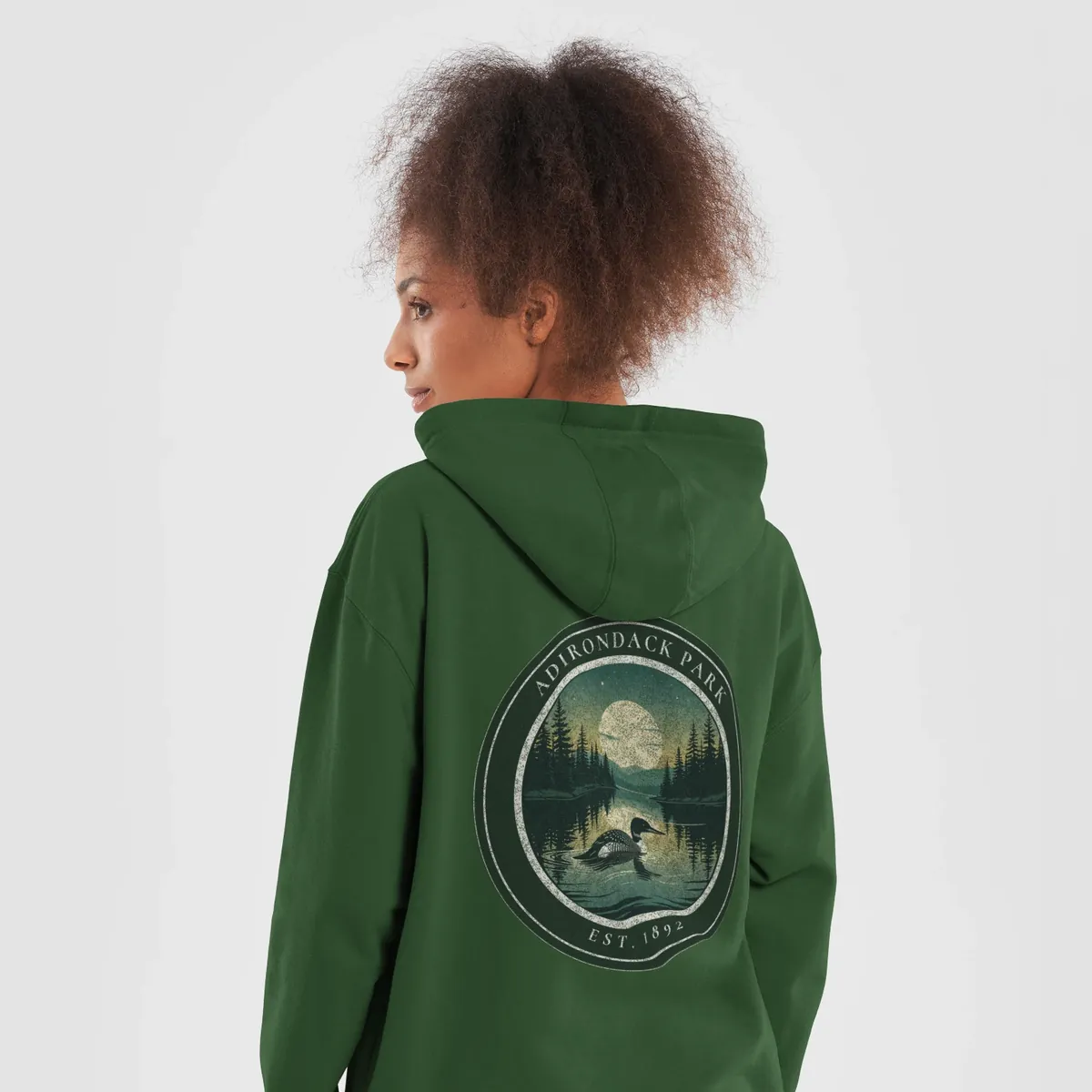 Loon at Night Hoodie in Forest Green, back: a loon on a moonlit Adirondack lake in a round badge, Adirondack Park, Est. 1892.