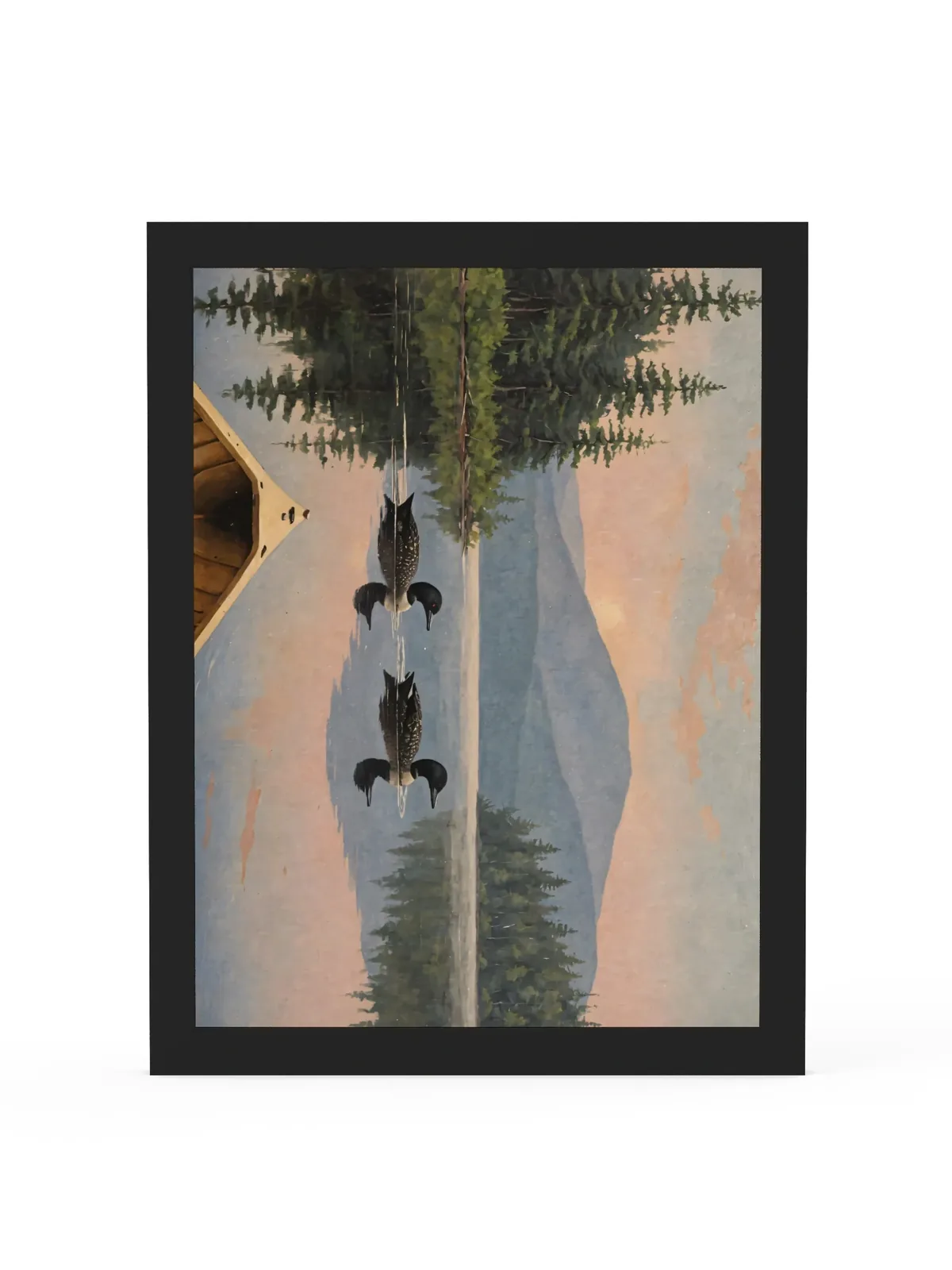 Loon Pair at Sunrise as a 12 by 16 inch framed print in a black frame: two common loons swimming side by side across a still Adirondack lake at sunrise, seen from the bow of a wooden canoe, with spruce shores, a blue mountain and a peach-pink sky doubled in the water, in soft, traditional oil brushwork.