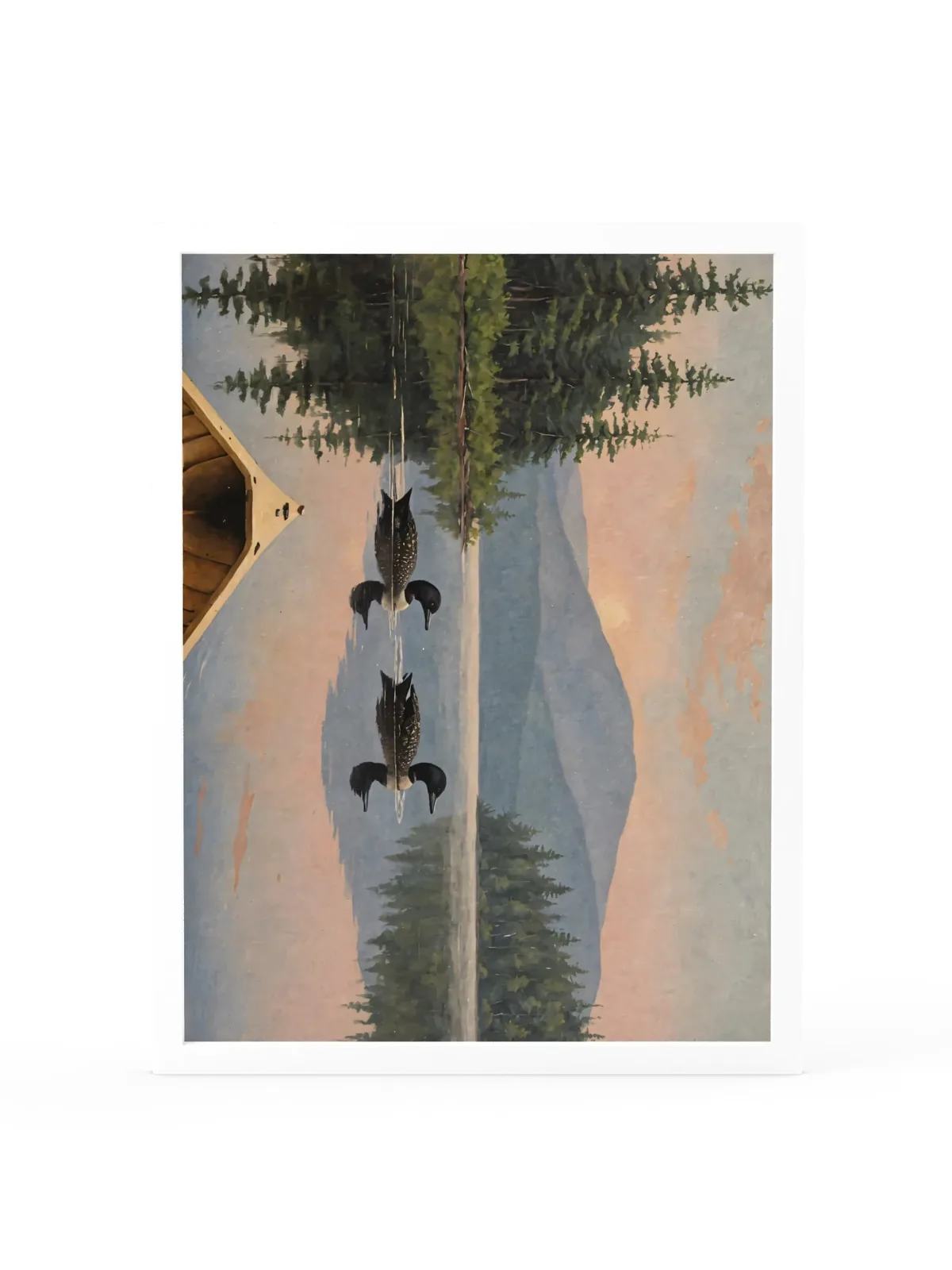 Loon Pair at Sunrise as an 18 by 24 inch framed print in a white frame: two common loons swimming side by side across a still Adirondack lake at sunrise, seen from the bow of a wooden canoe, with spruce shores, a blue mountain and a peach-pink sky doubled in the water, in soft, traditional oil brushwork.